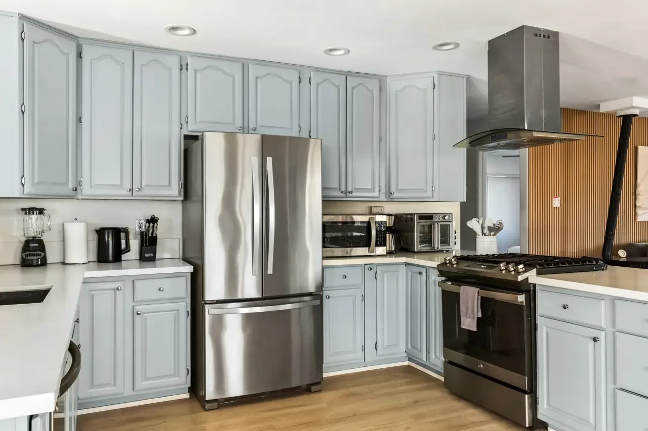 Kitchen with light blue cabinets, stainless steel refrigerator, black oven, microwave, toaster oven, and kitchen appliances.