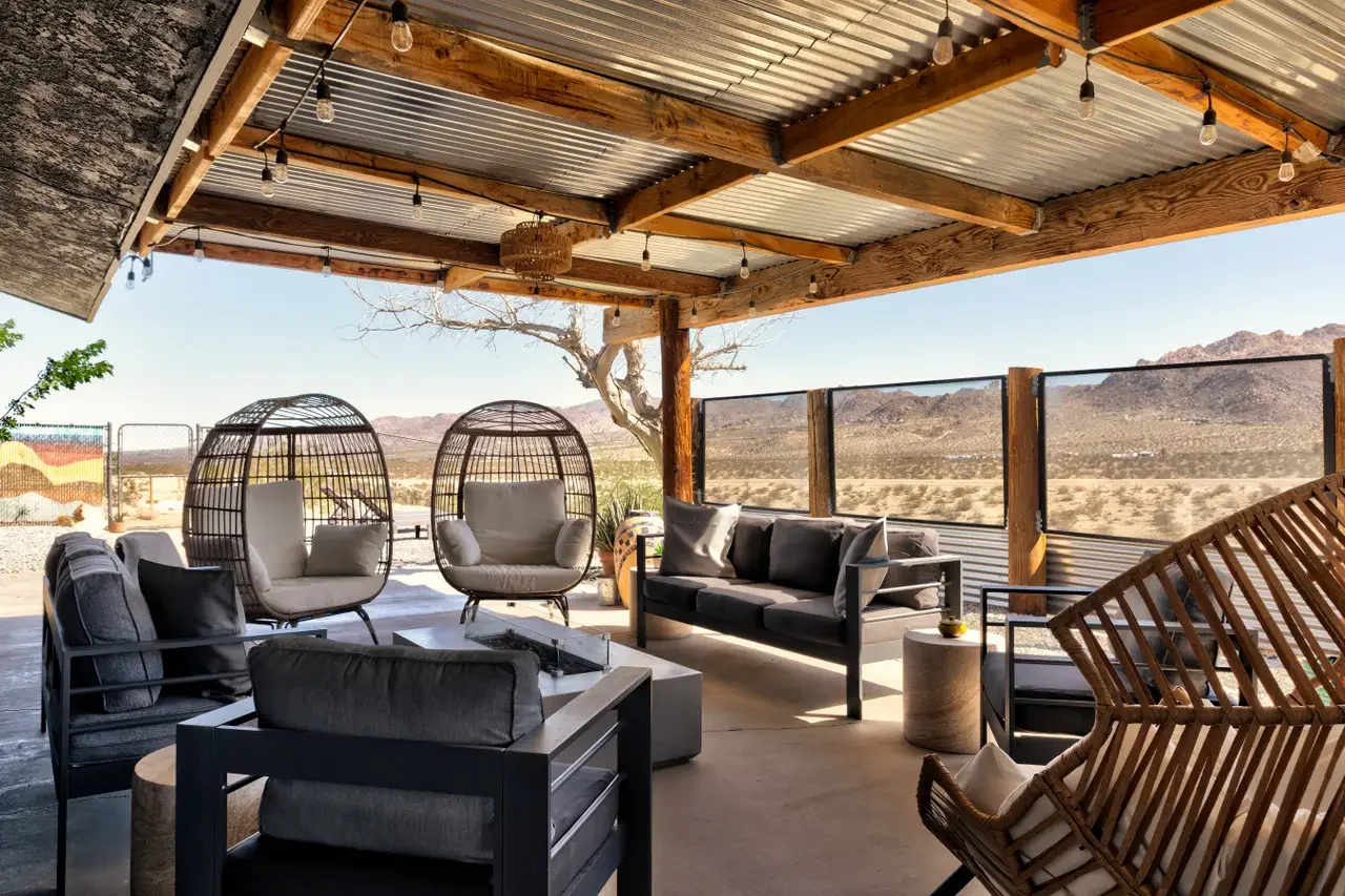 Outdoor patio with modern black and gray seating, two papasan chairs, wicker accents, string lights, and a view of desert landscape and mountains in the background.