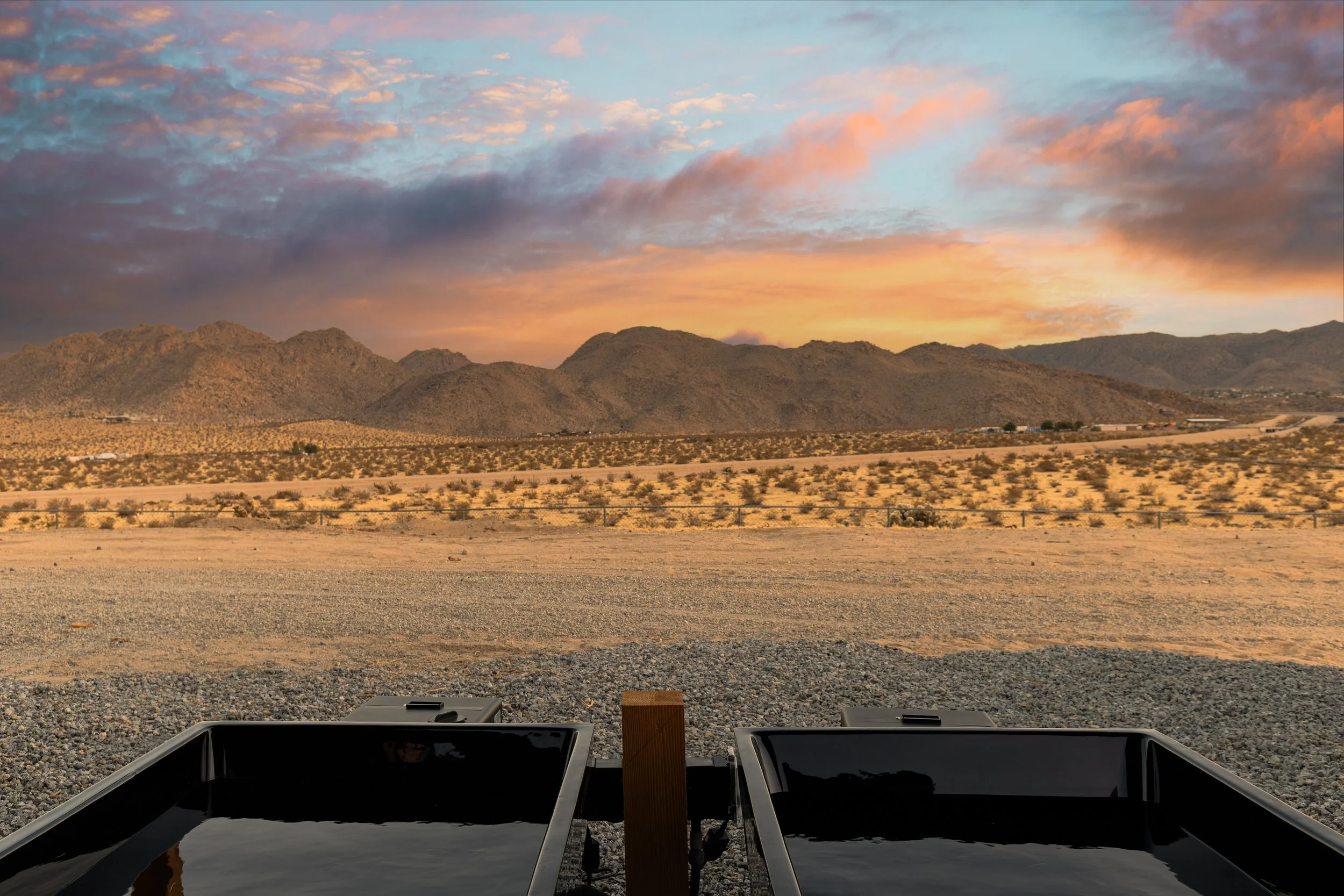 View of desert landscape with mountains at sunset, seen from a shaded area with picnic tables in the foreground.