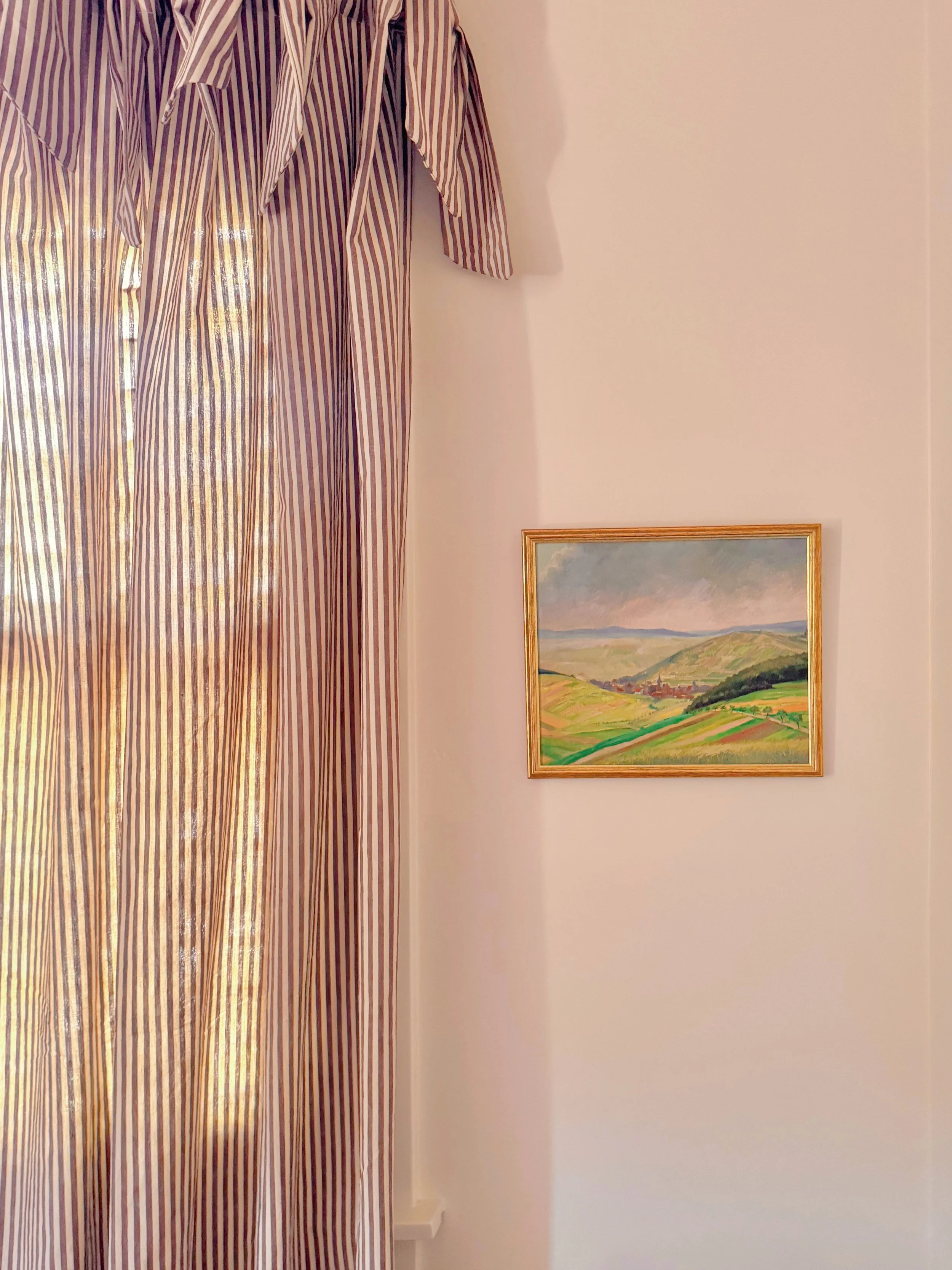 A room with a striped curtain on the left and a framed painting of a landscape on the right wall.