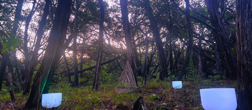 Sunrise in a dense cedar forest with a 3 foot wooden boat ornament and illuminated crystal bowls in the foreground.