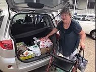 Older man with gray hair loading groceries into the trunk of a silver SUV, using a walker for support.