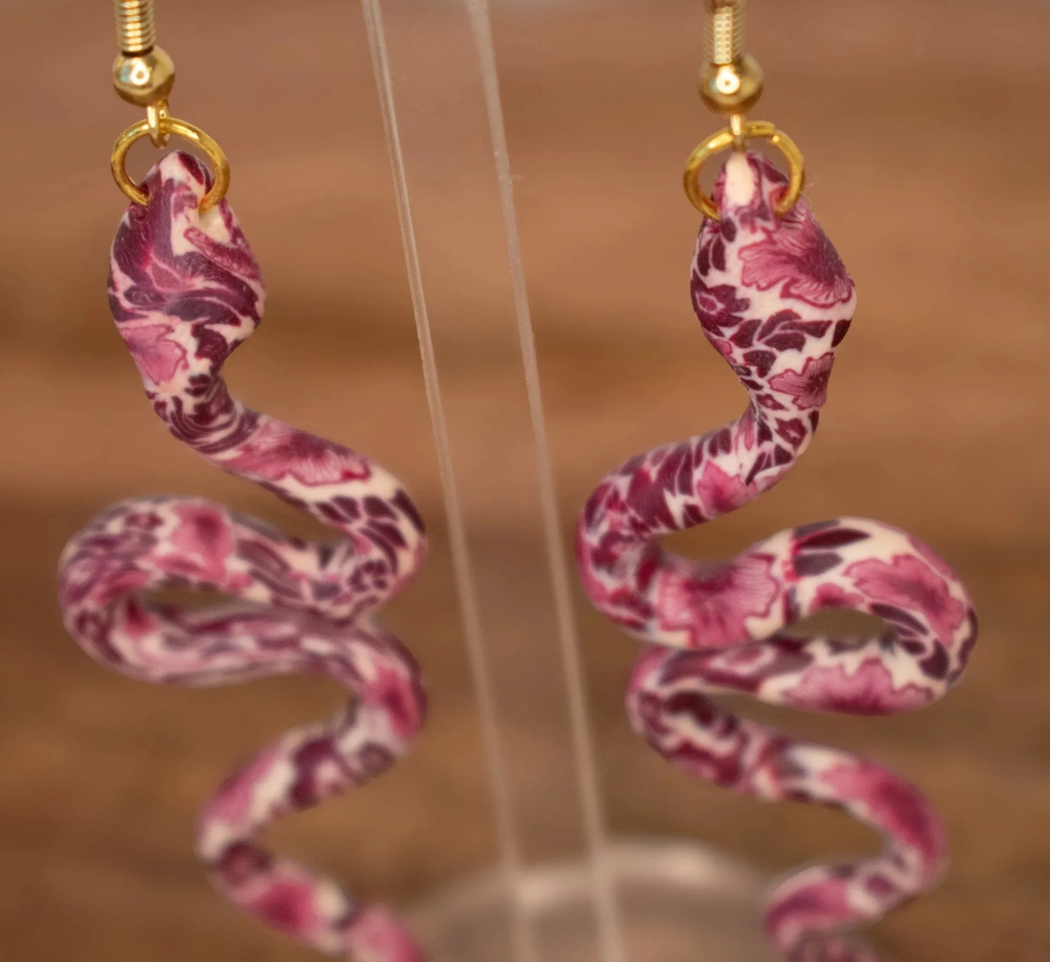 Close-up of a pair of earrings with pink and white marble designs hanging from a display stand.