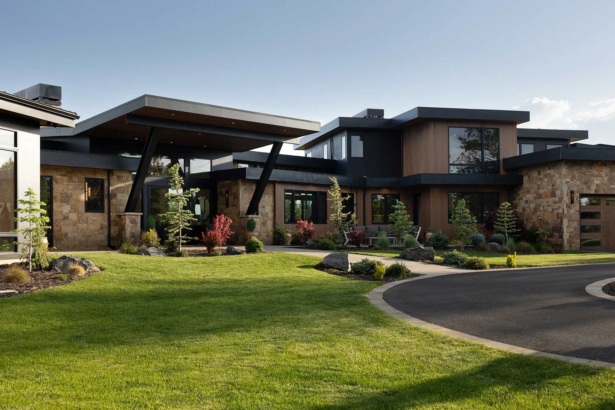 Front exterior of a contemporary custom home with stone walls, wood siding and a covered entry in The Highlands at Broken Top.