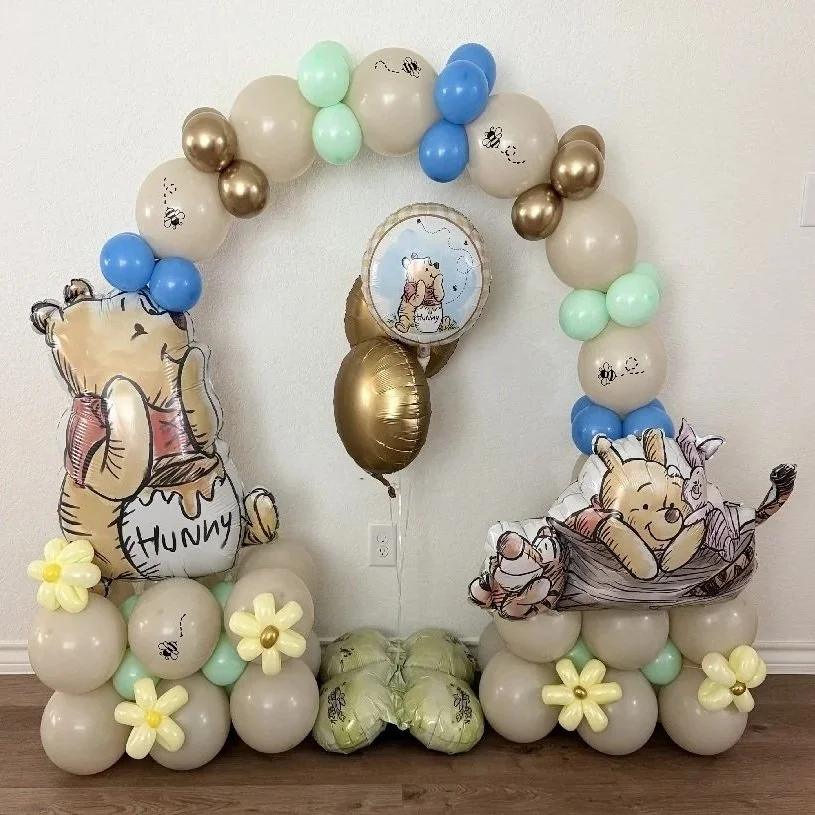 Balloon arch with Winnie the Pooh themed decorations, including balloons, characters, and flowers for a celebration.