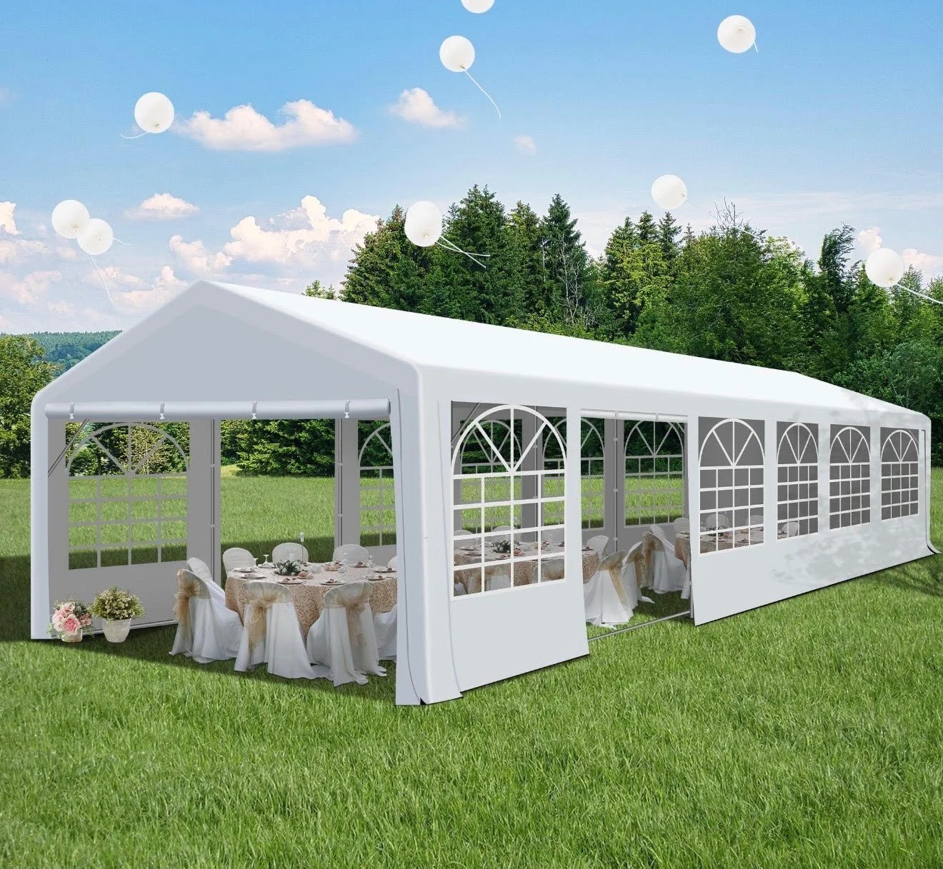 White event tent set up outdoors on grass, decorated with tables and chairs for a celebration, with balloons floating in a blue sky with clouds and trees in the background.