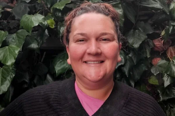 A woman smiling in front of a leafy green background.