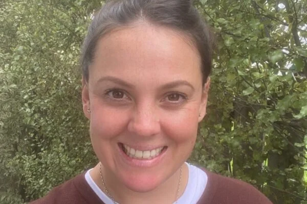 Close-up of woman smiling outdoors with green foliage background.
