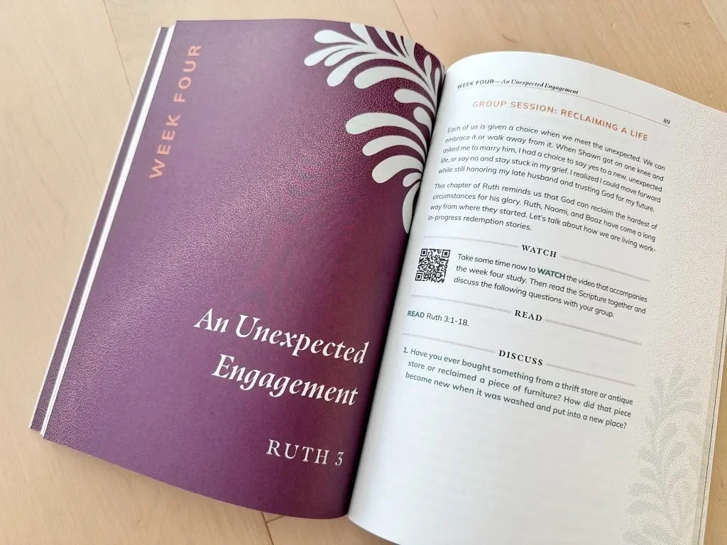 Open book titled 'An Unexpected Engagement' from week four, with a purple cover featuring white foliage design, resting on a wooden surface. The pages include a group session discussion, watch, read, and discuss sections for Ruth 3.