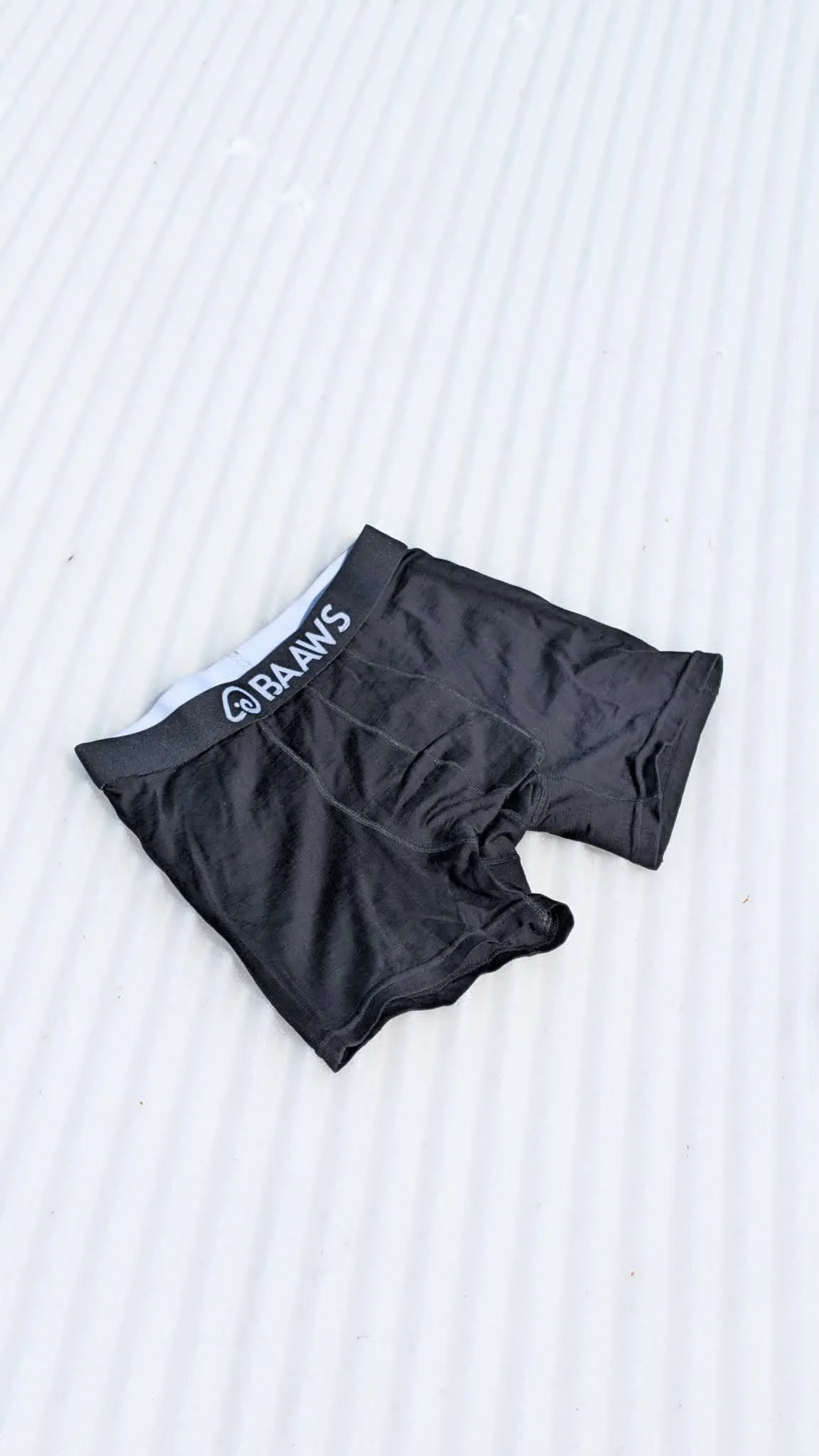 Black men's briefs and "BAAWS" printed on the waistband in white, lying on snow