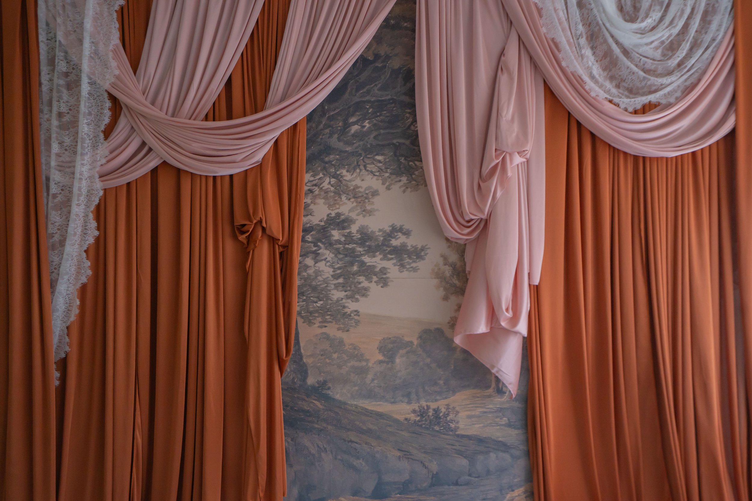 Pink and orange curtains draped around a wall with a landscape mural of trees and mountains.