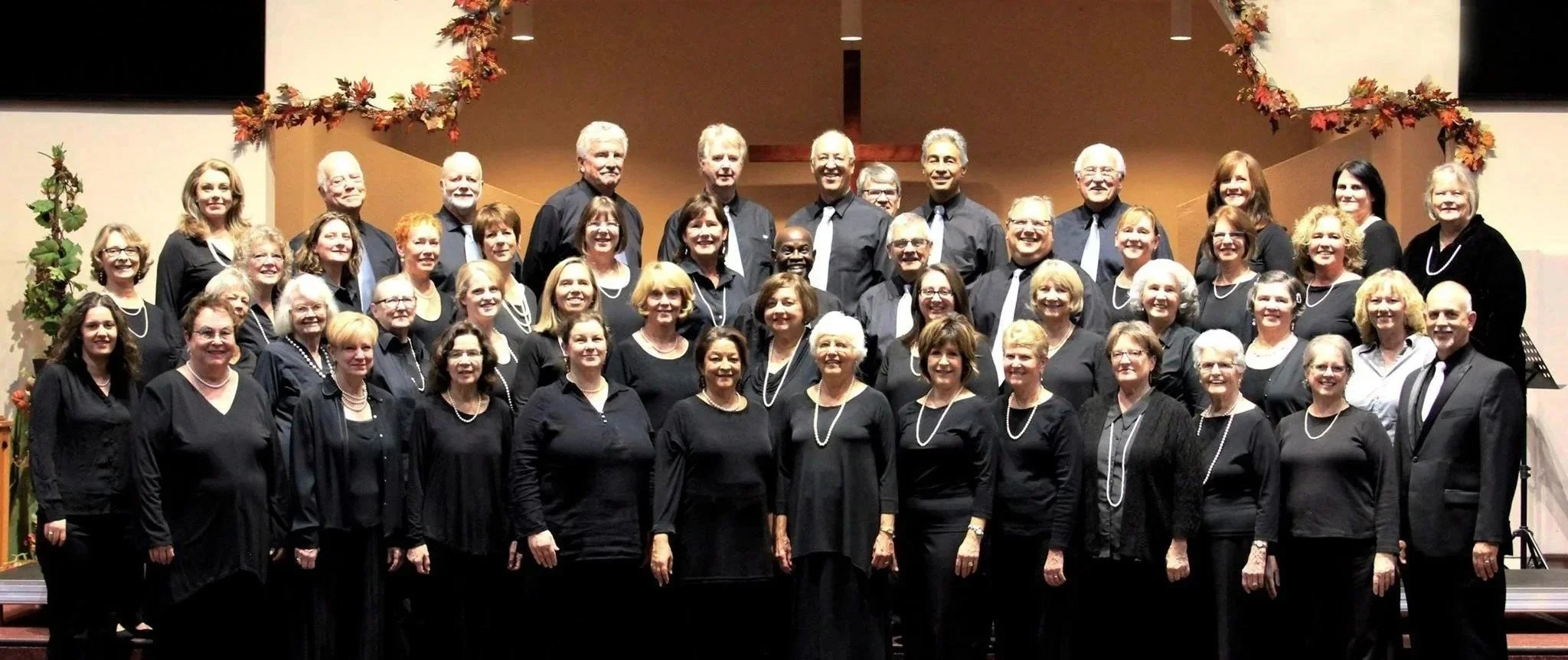Group photo of choir members dressed in black, standing on stage with holiday decorations.