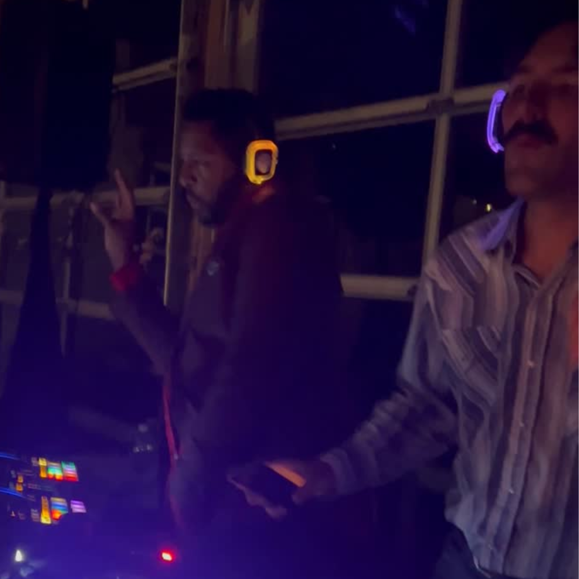 A neon-lit indoor scene with people, some wearing glowing bracelets, and a mirror reflecting their faces. The environment has a dark, vibrant atmosphere.