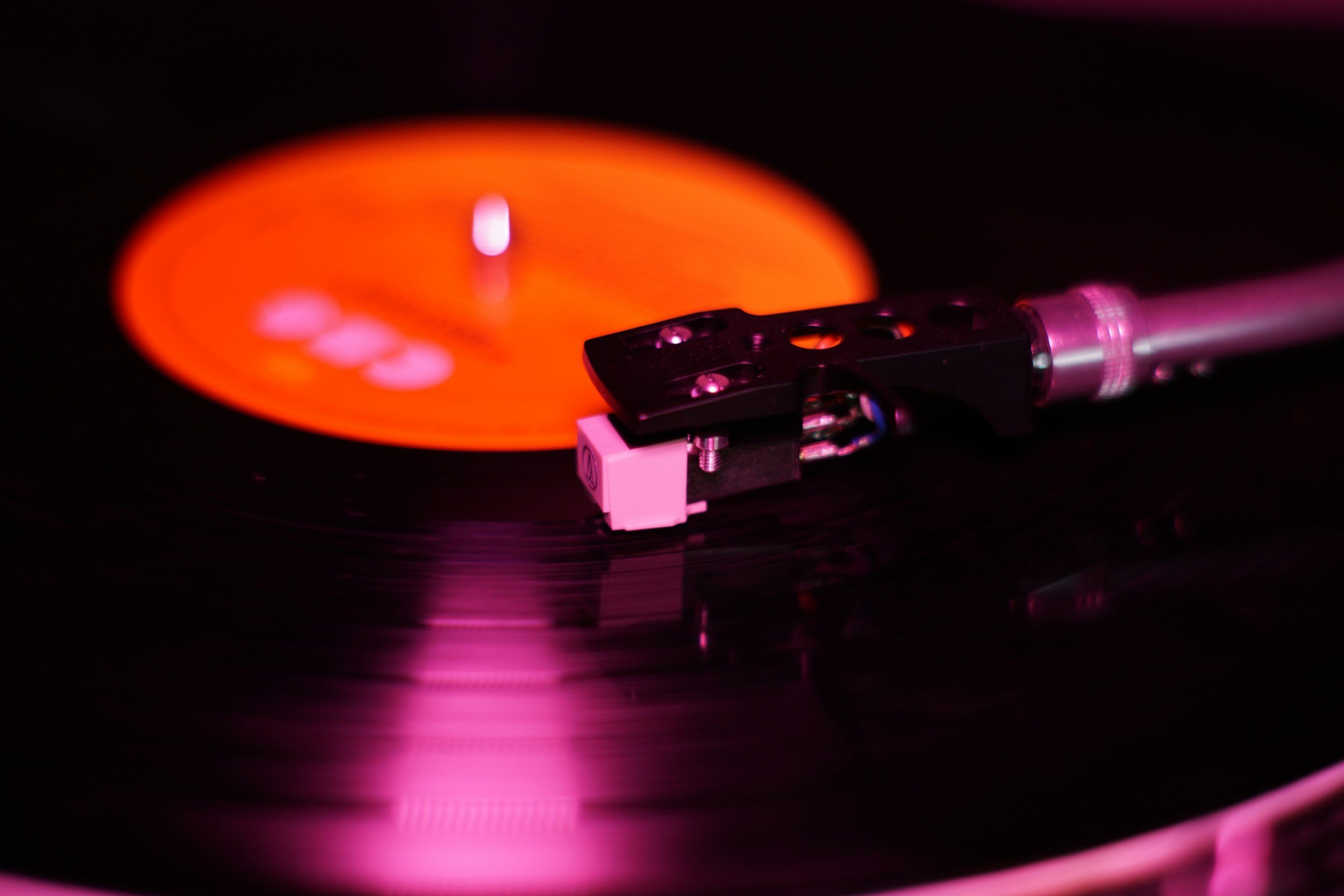 Close-up of a vinyl record spinning on a turntable with pink lighting, focusing on the turntable's tonearm and stylus.