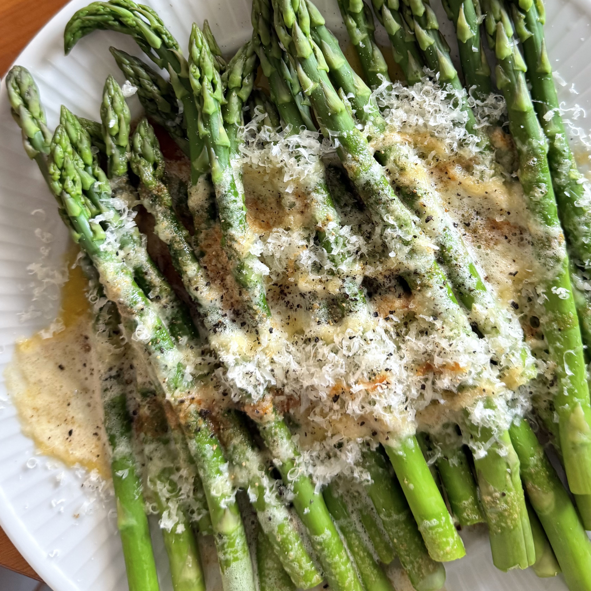 Fresh green asparagus spears being cooked, with grated cheese on top.