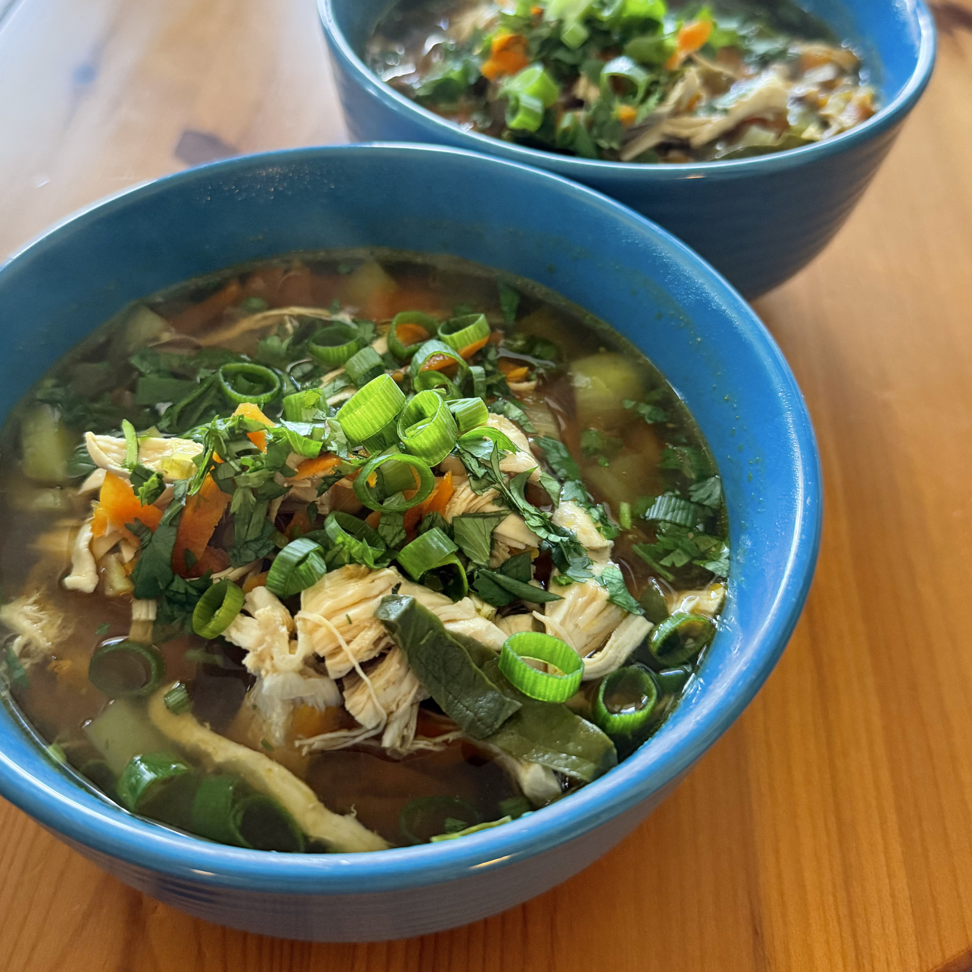 Bowls of hot homemade chicken vegetable soup garnished with chopped green onions on a wooden table.