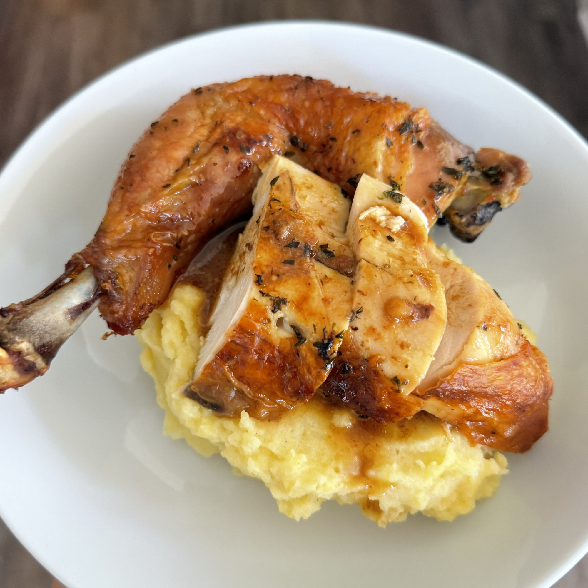 A close-up of baked chicken with herbs served over mashed potatoes on a white plate.