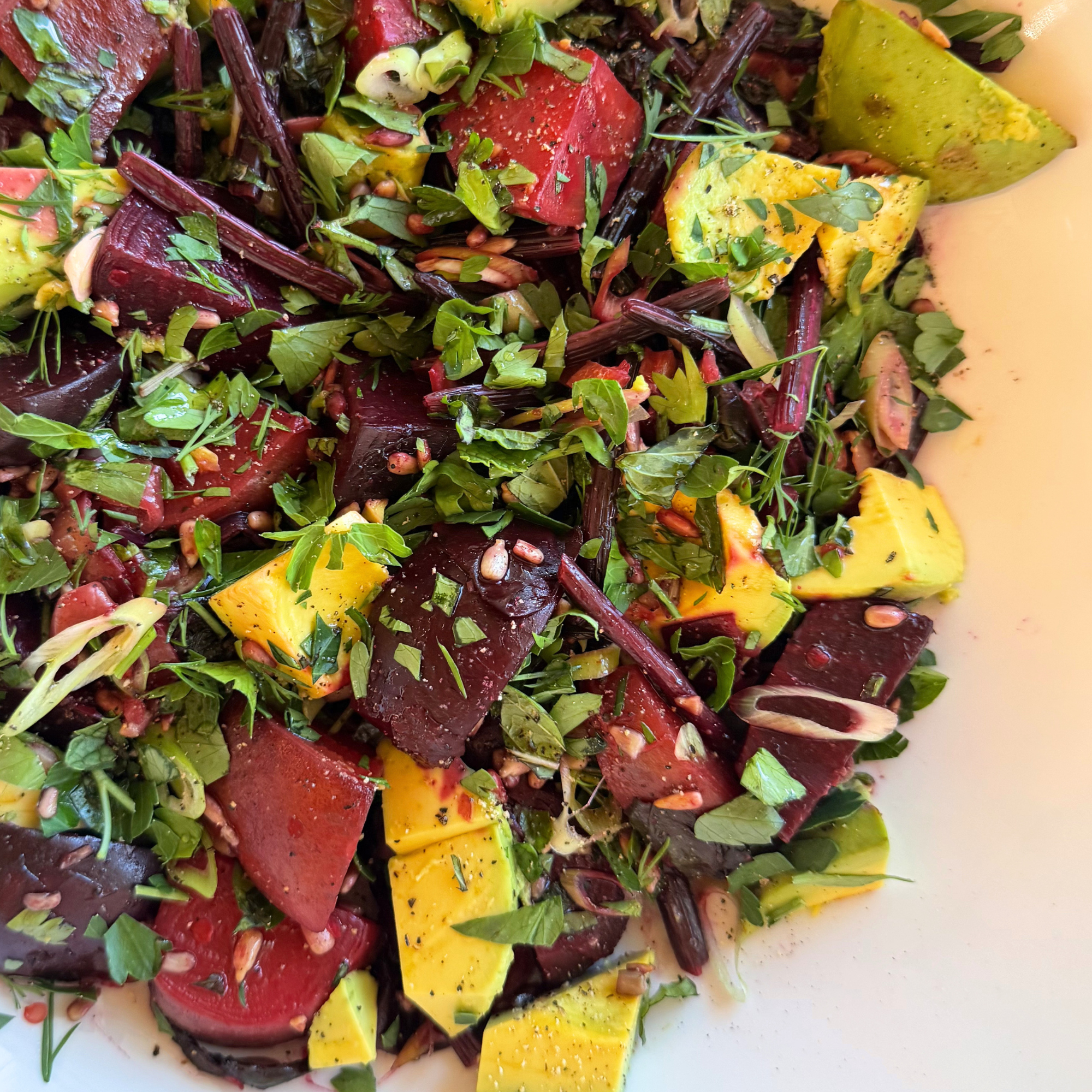 Close-up of a colorful salad with sliced beets, mango, and greens on a white plate.