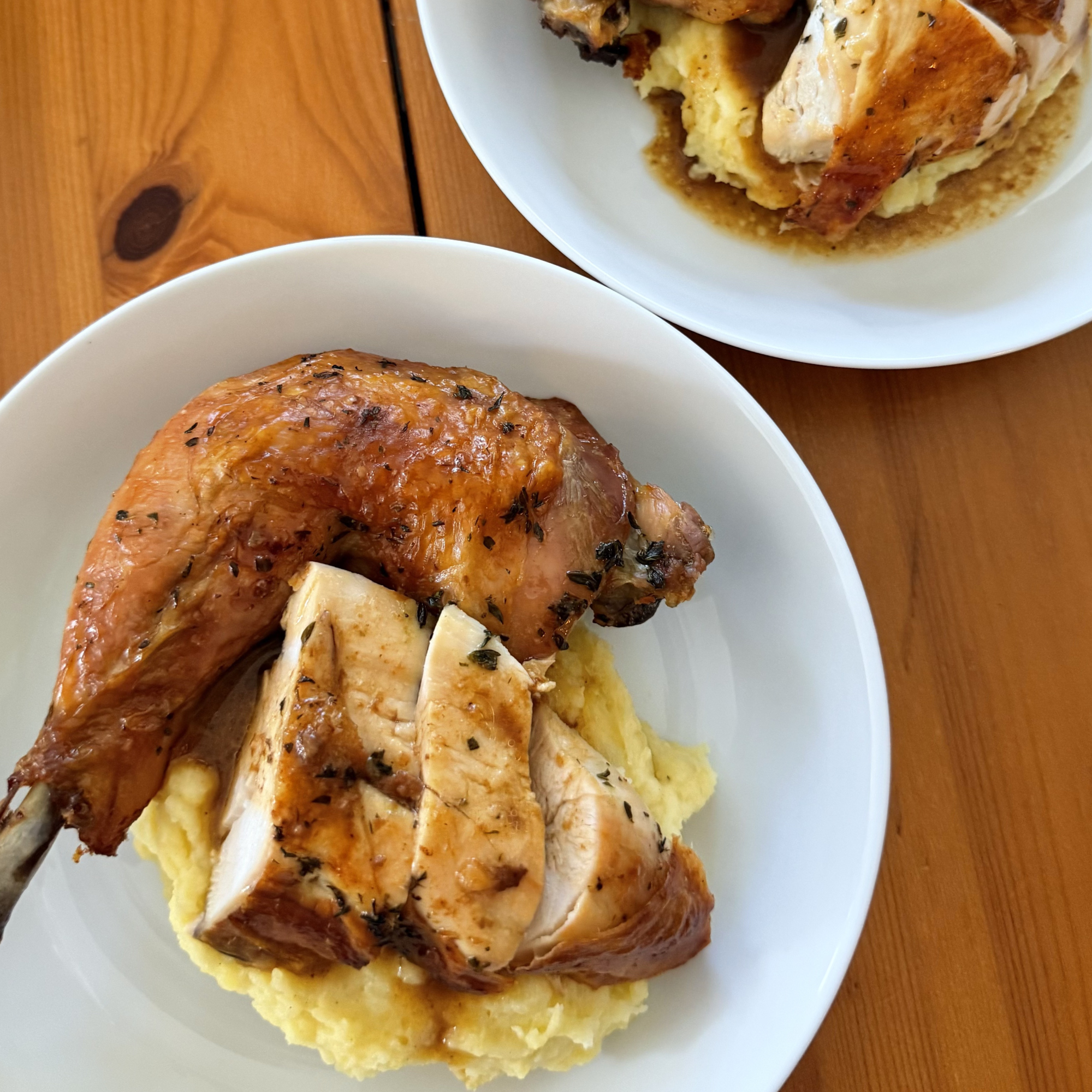 Roasted chicken breast with herbs served over mashed potatoes on a white plate, resting on a wooden table.