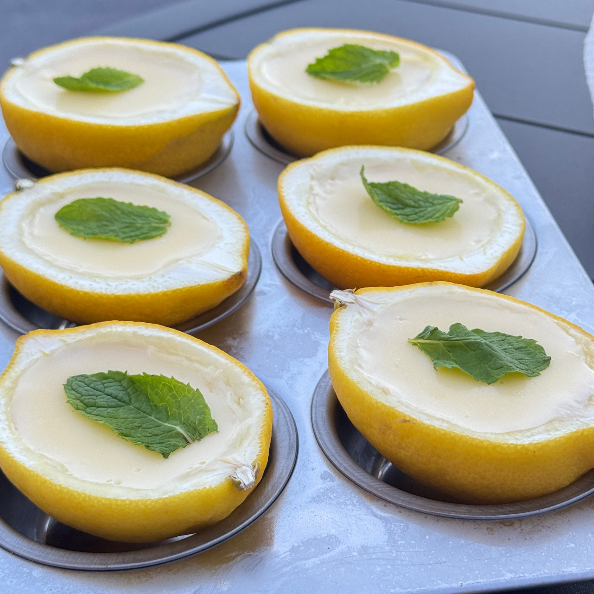 Halved lemons filled with lemon curd or custard, garnished with fresh mint leaves, arranged on a tray.