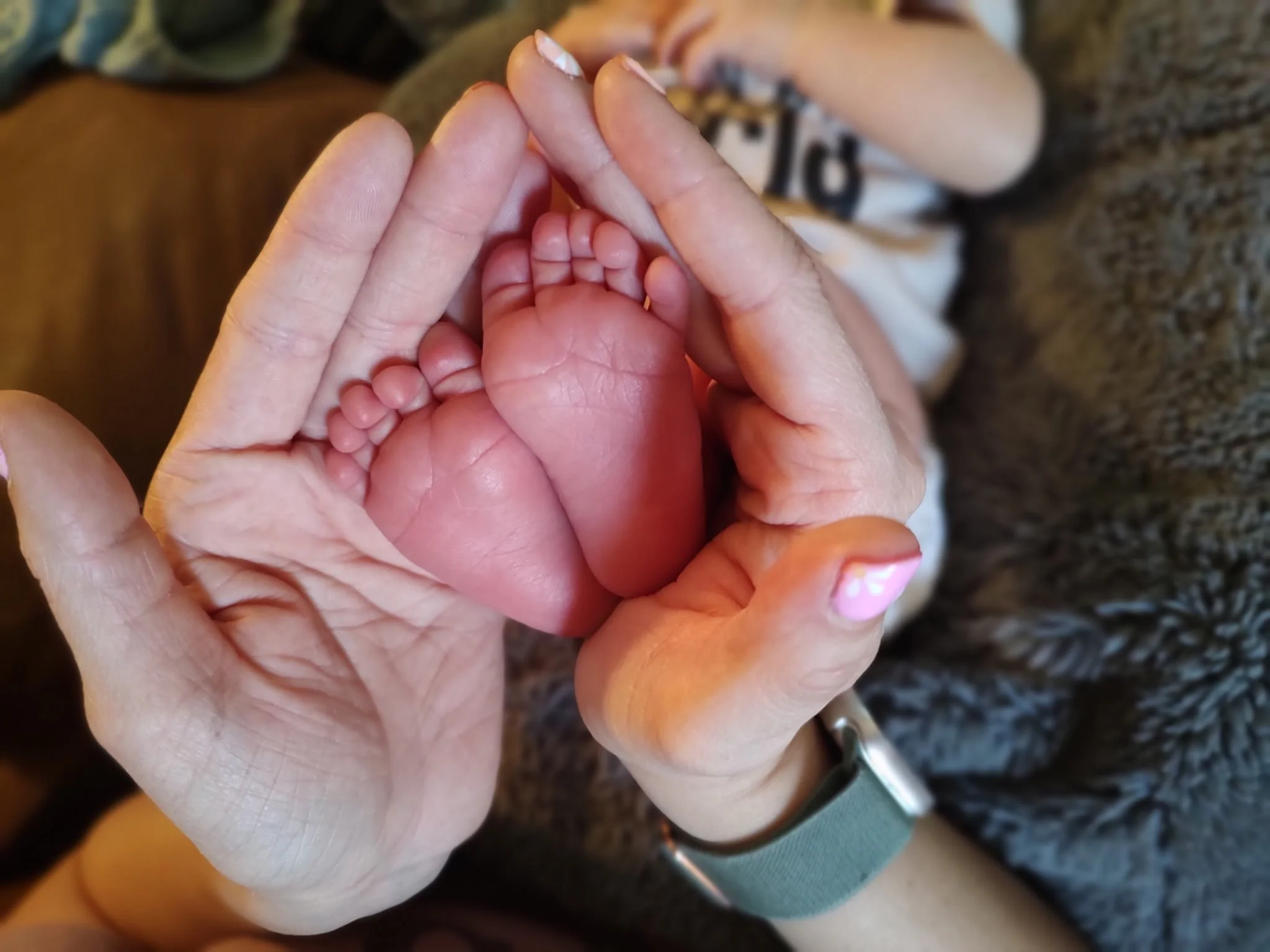 Close-up of an adult's hand gently holding a small baby’s toes, with the background slightly blurred.