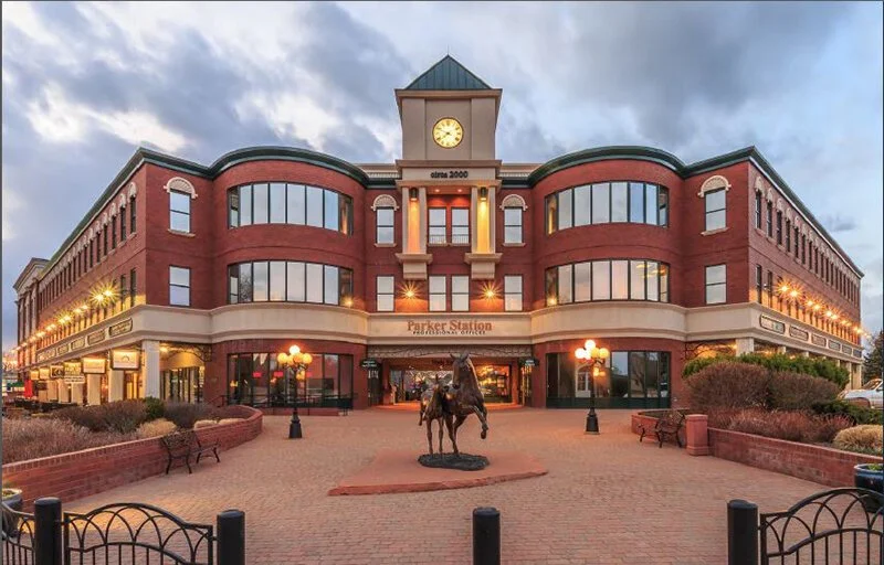 A three-story brick building with a clock tower on top, titled Parker Station, with an equestrian statue in front and a brick plaza.