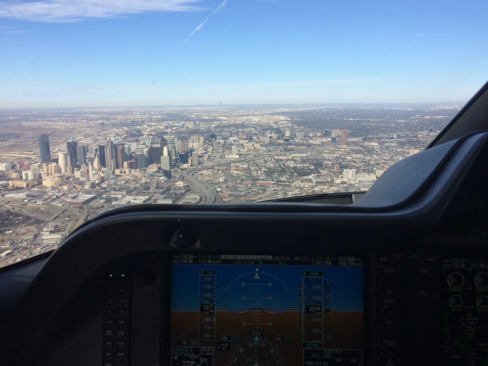 An aerial view of a cityscape with numerous buildings, highways, and clear skies, seen from the cockpit of an airplane.