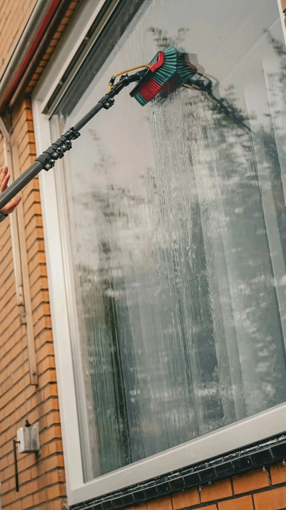 A person is pressure washing a large window on a brick building.