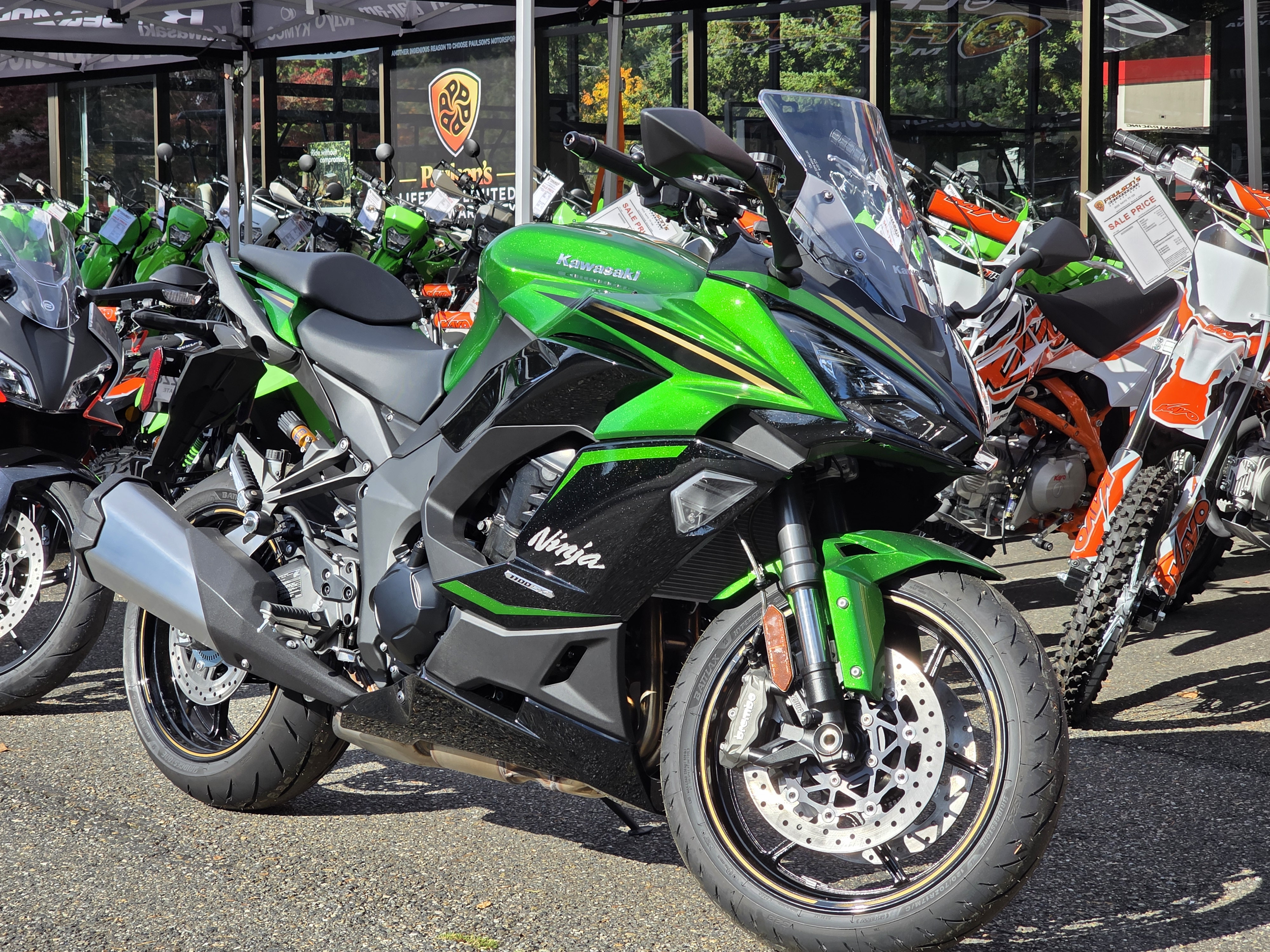 Multiple motorcycles on display outside of DFD CYCLES, with a focus on a bright green Kawasaki Ninja in the foreground.