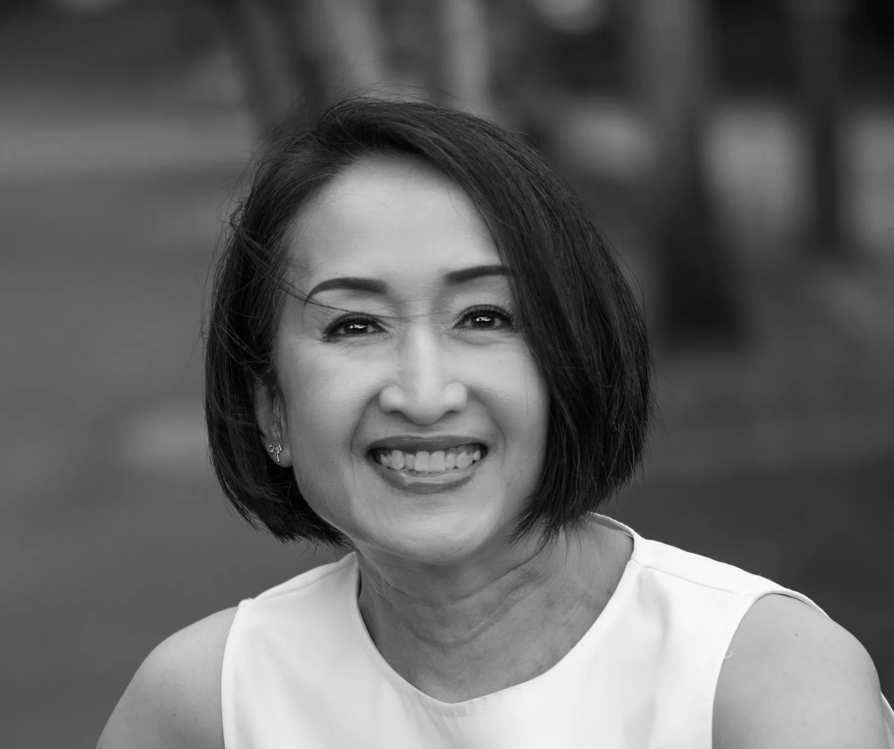 Black and white photo of a cheerful woman with short, dark hair, smiling and showing her teeth, wearing a sleeveless top.
