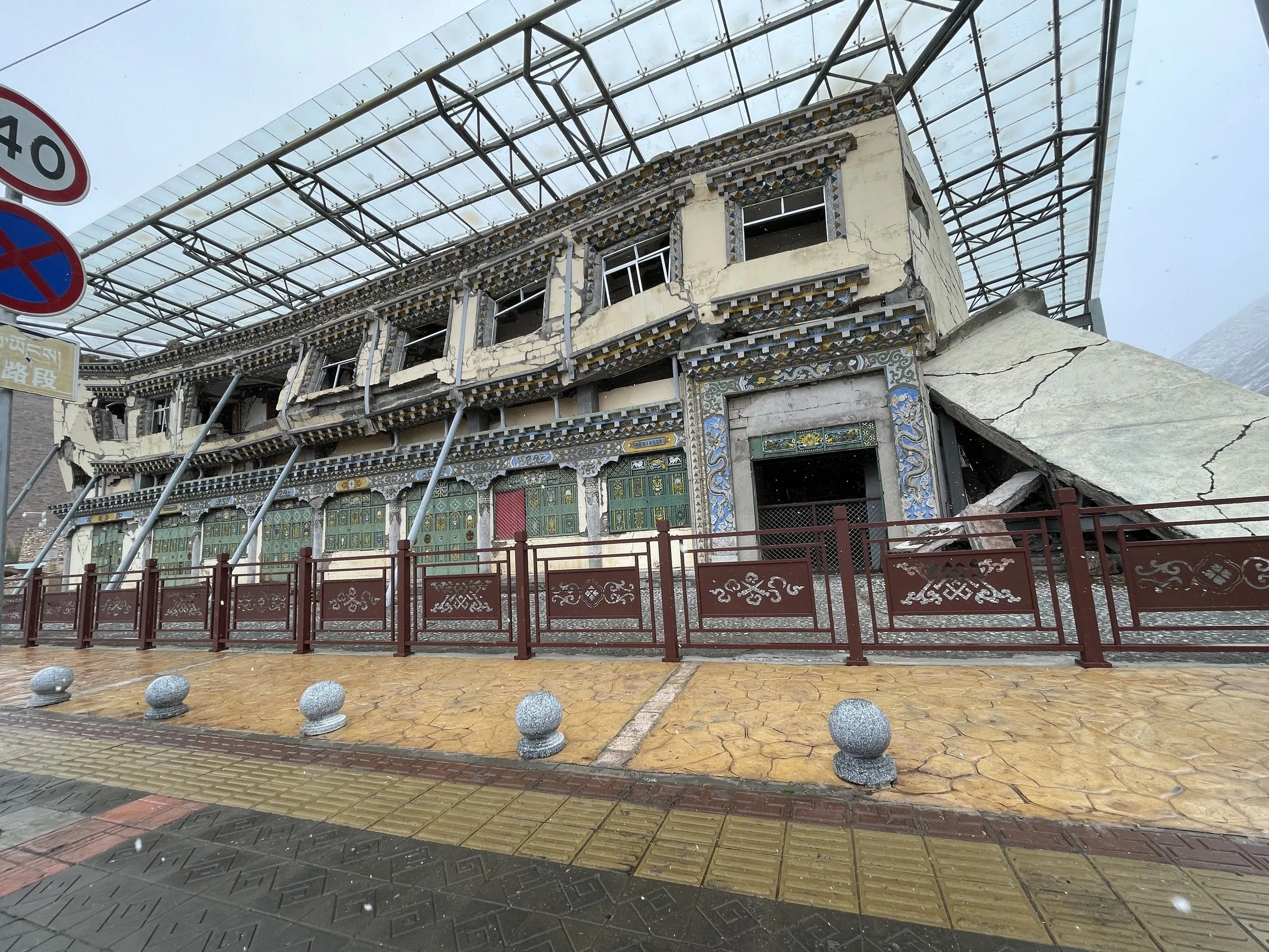 "The preserved ruins of the Yushu Earthquake Memorial Site in Qinghai, showing a standalone building with a collapsed center left as a historical monument."