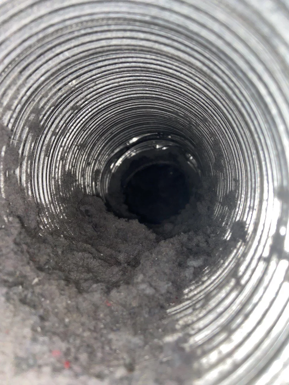 Inside of a metal pipe with dirt and debris at the bottom.