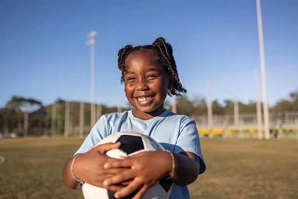 Young girl smiling and holding a soccer ball on a field.