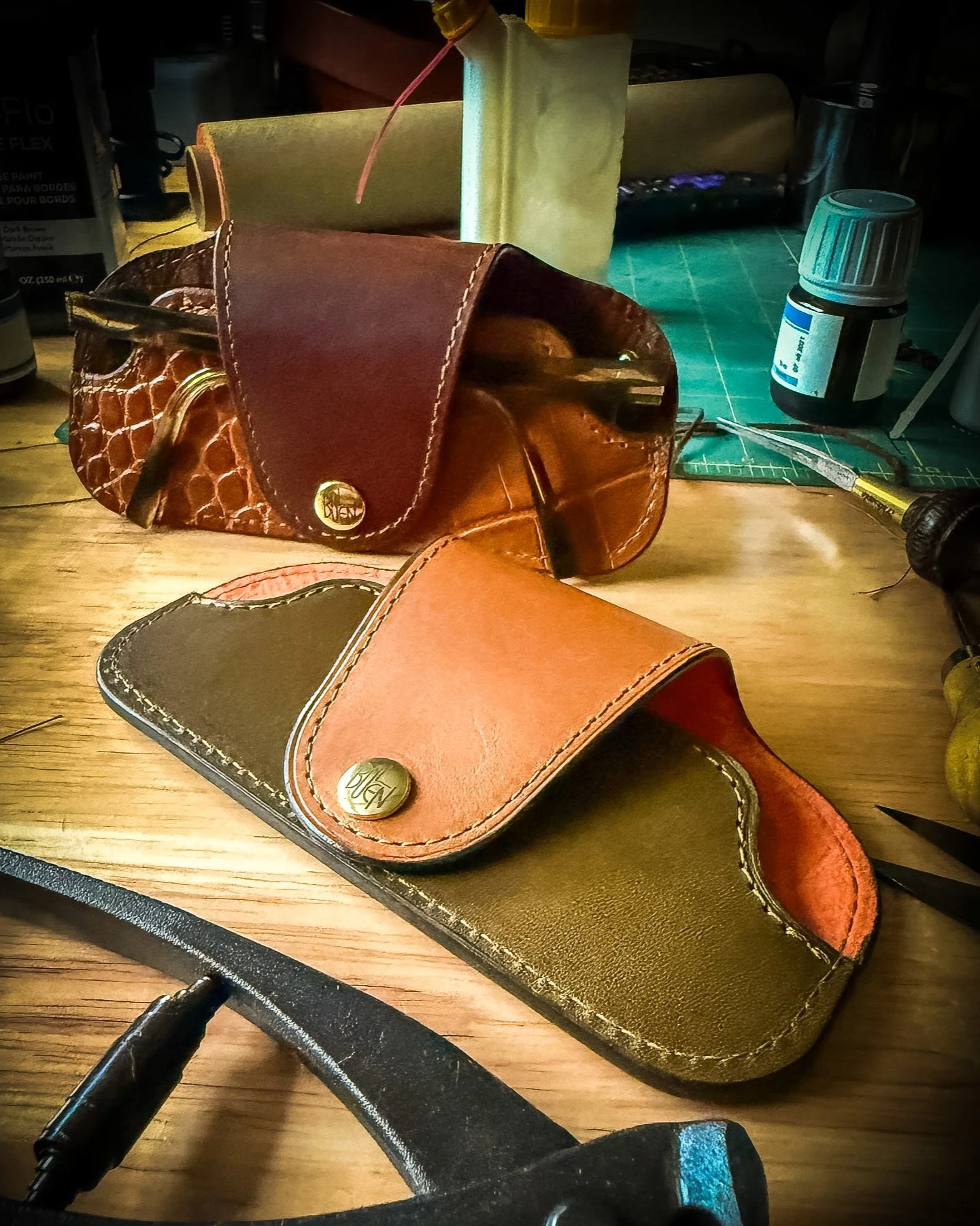 Various two-tone slimline glasses cases on a wooden table, with some tools and supplies in the background.