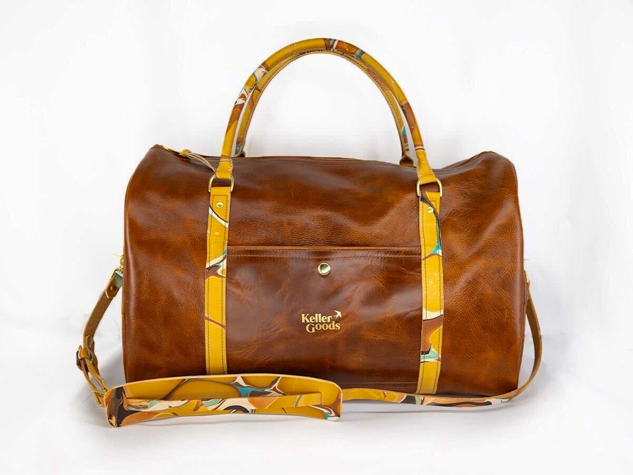 A brown leather duffel bag with yellow and multicolored patterned handles and straps, branded with 'Keller Goods' in gold lettering on the front, set against a plain white background.