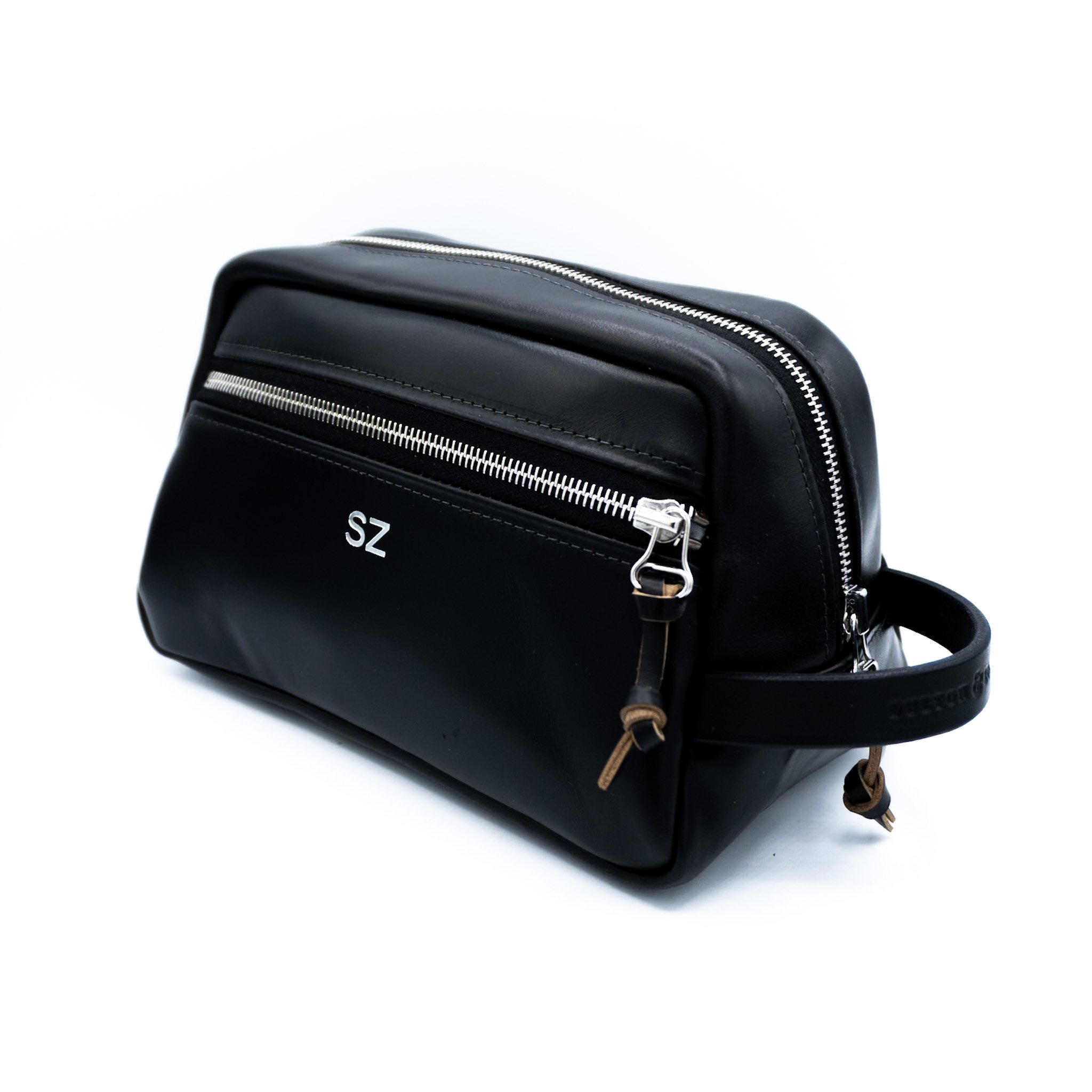 Close-up of a black leather backpack with silver zippers and brown leather drawstrings against a white background.