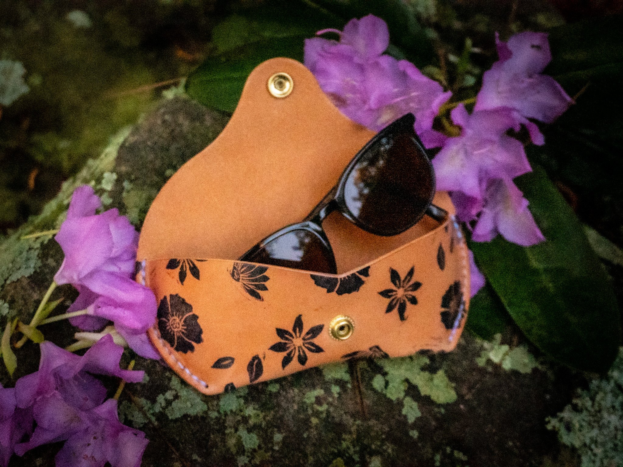 Orange box with black floral pattern, sunglasses, and purple flowers around it.
