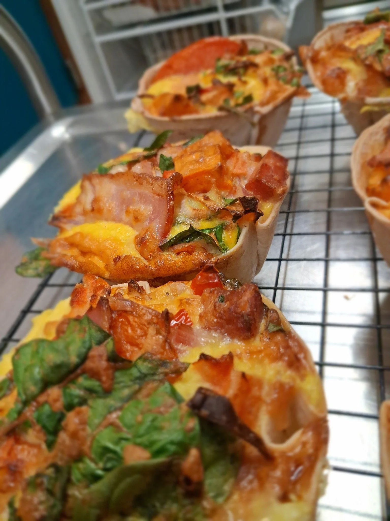 Slices of vegetable pizza with toppings like spinach, tomatoes, and cheese on a wire rack.