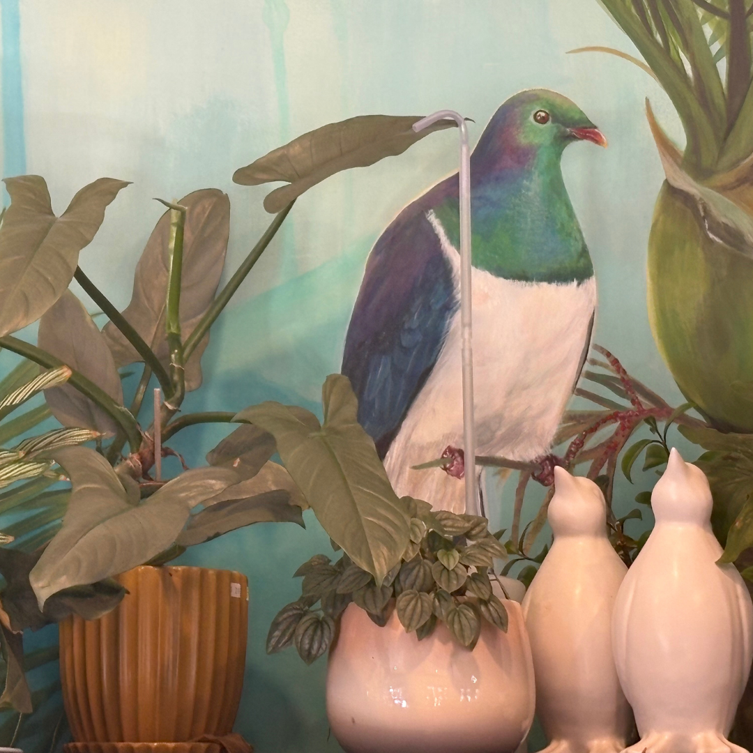 Wall mural of a colorful pigeon surrounded by potted plants and decorative white ceramic figures.