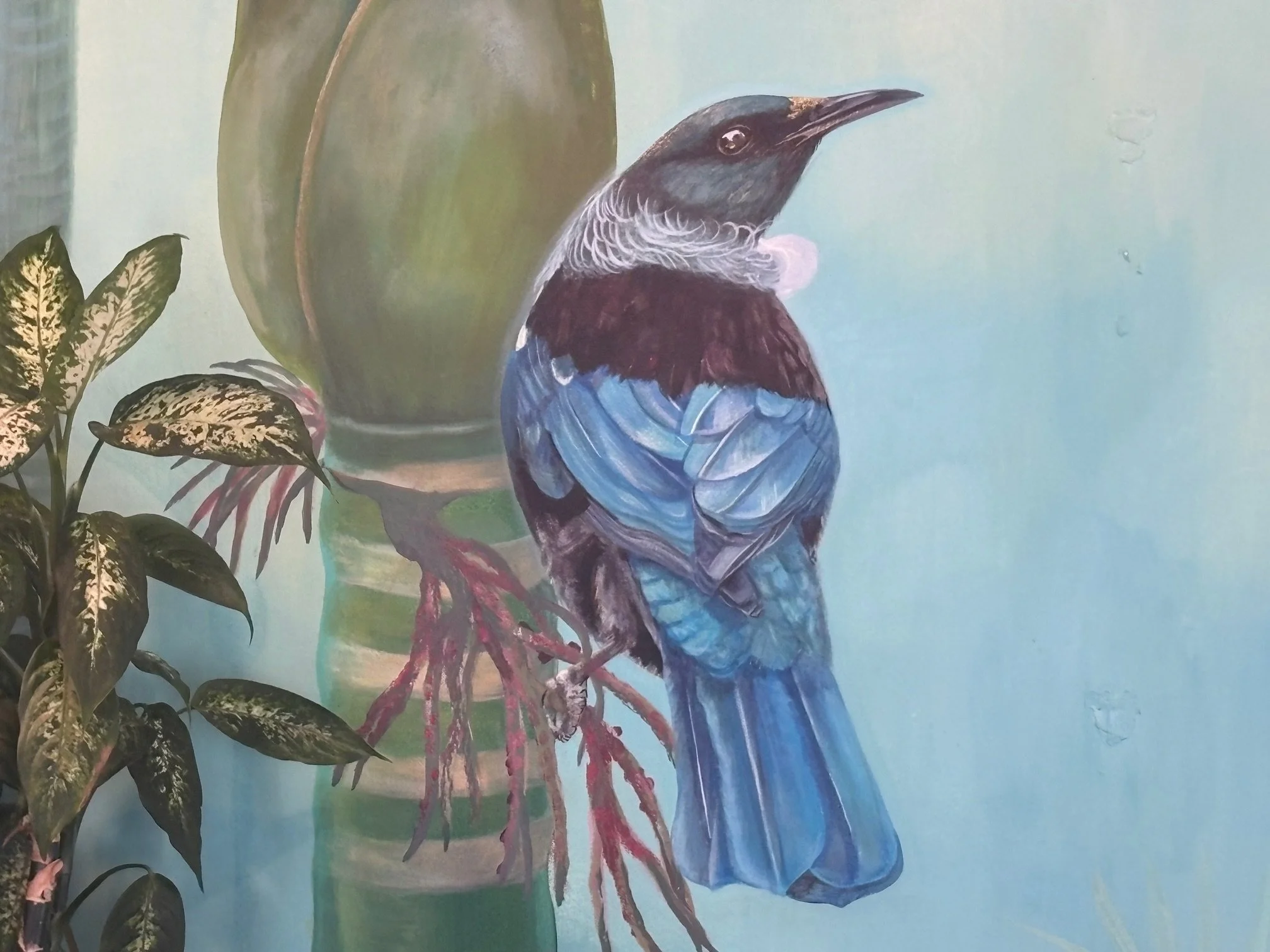 Painting of a bird perched on a branch next to large green and variegated leaves with a blue background.