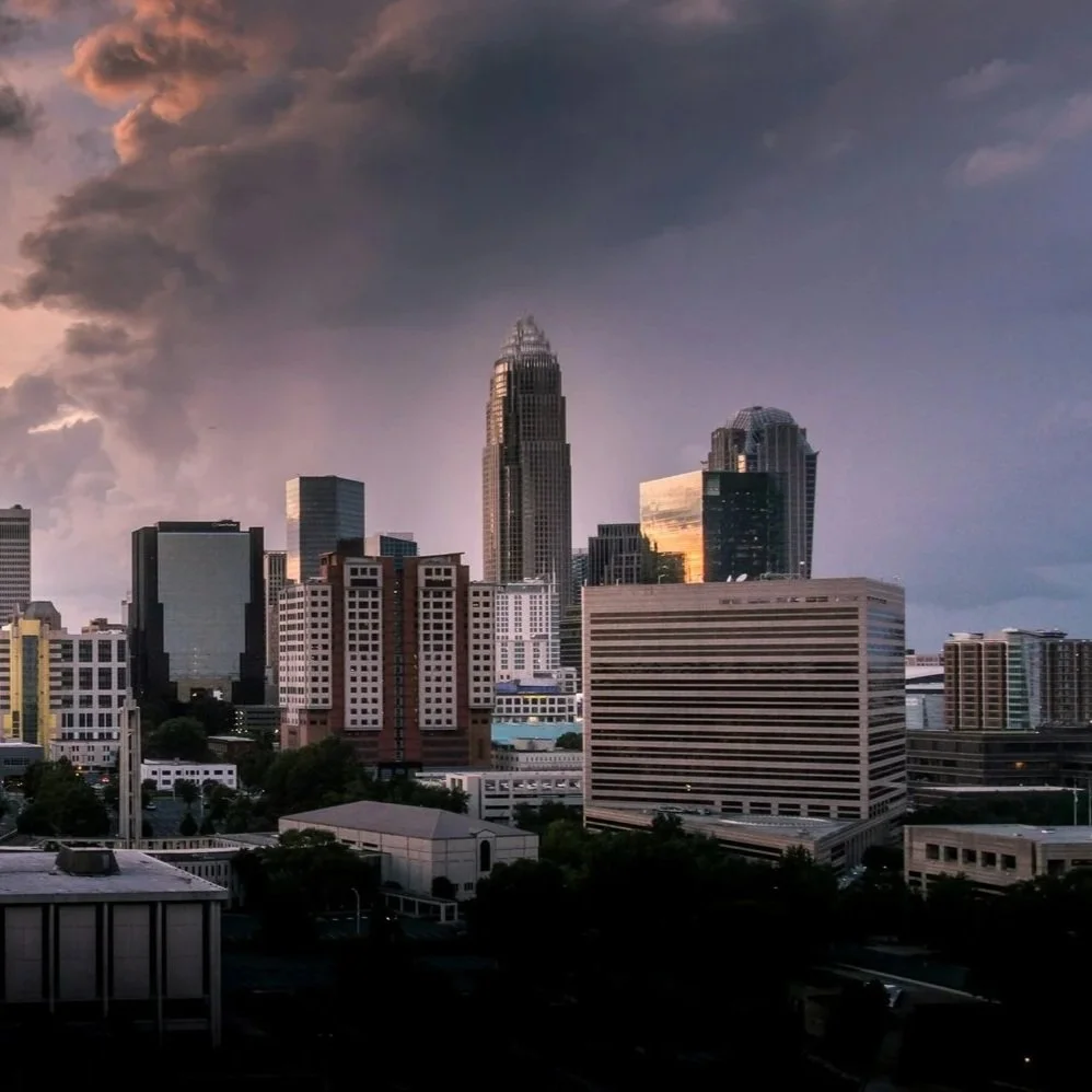 The skyline of a city with tall buildings and a dramatic darkening sky with storm clouds.