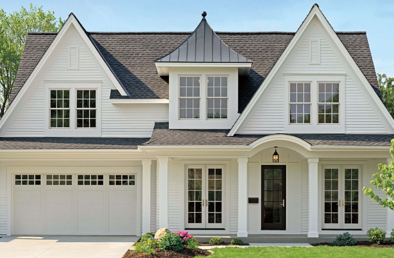 Front view of a white two-story house with dormer windows, a black front door, and a landscaped yard.