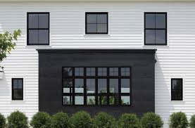 Modern white house with large central window and black accents, surrounded by greenery.