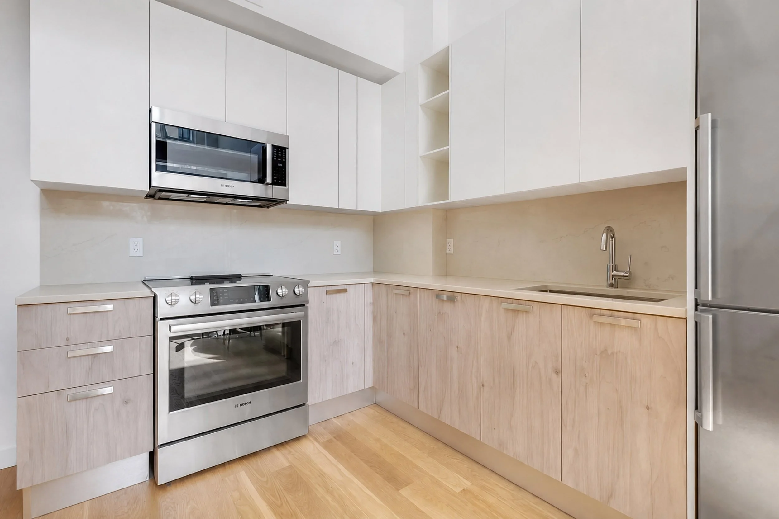 	The original kitchen — white upper cabinets, pale timber below, stone benchtop and stainless appliances