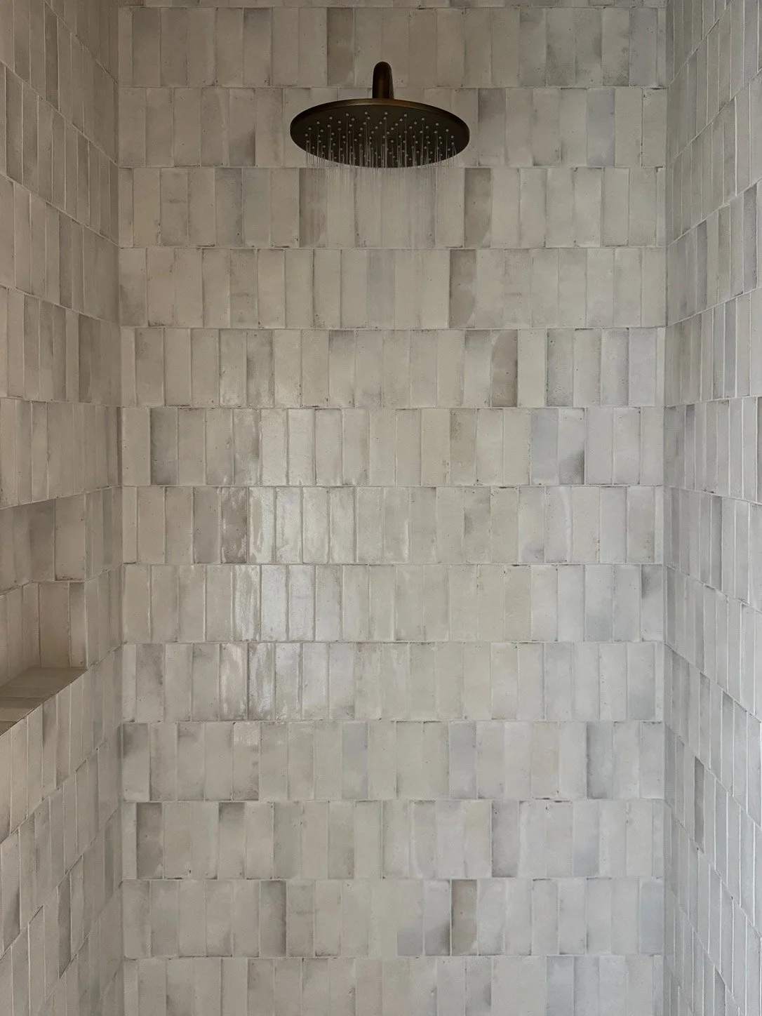 Shower lined in handmade zellige tile with an aged brass rain head