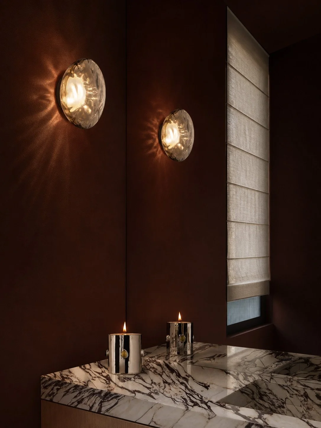 Powder room in deep oxblood with textured glass disc sconces above a Calacatta Viola vanity