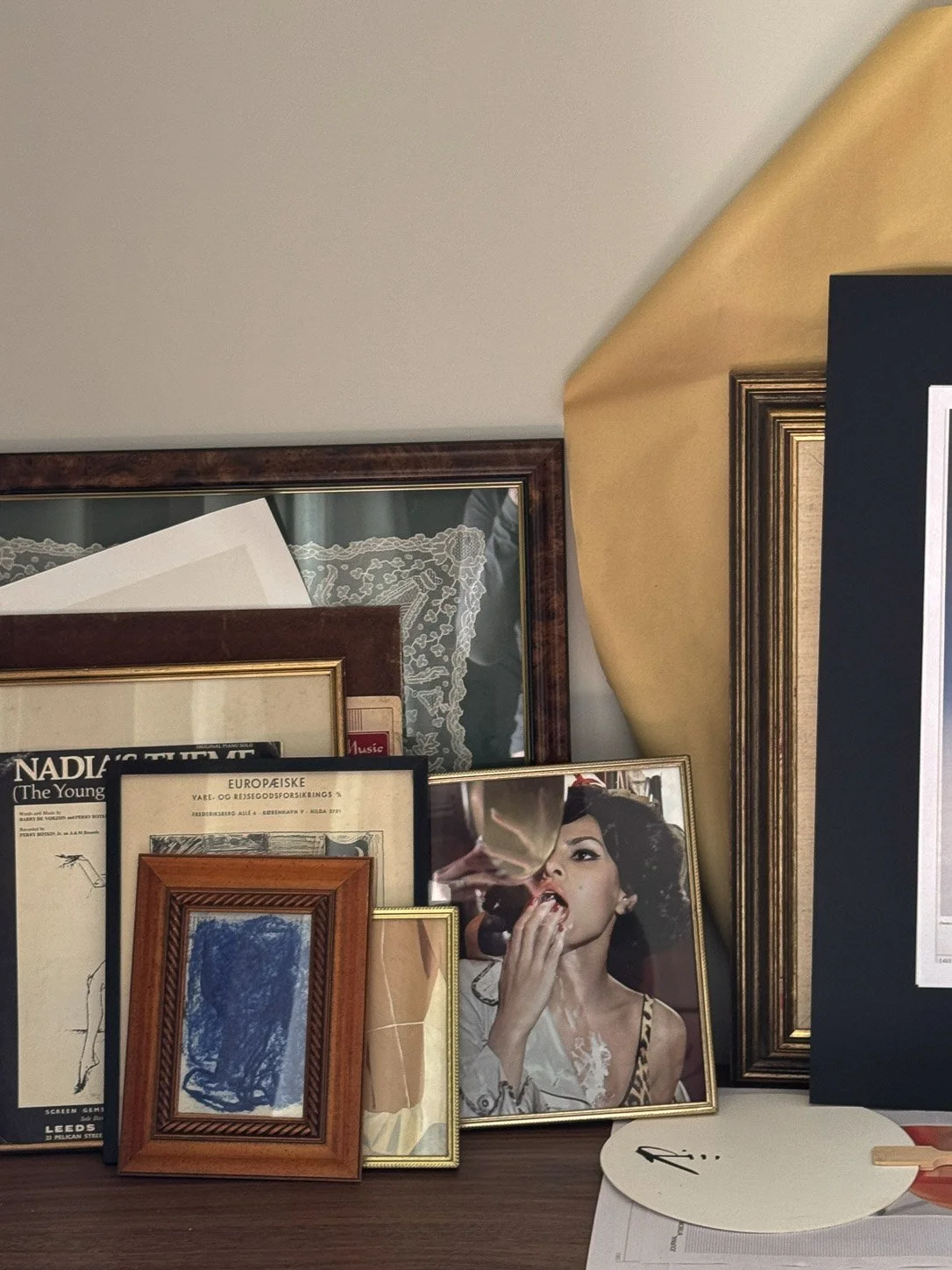 Framed pieces stacked on a walnut cabinet — vintage sheet music, a blue abstract, a fashion photograph