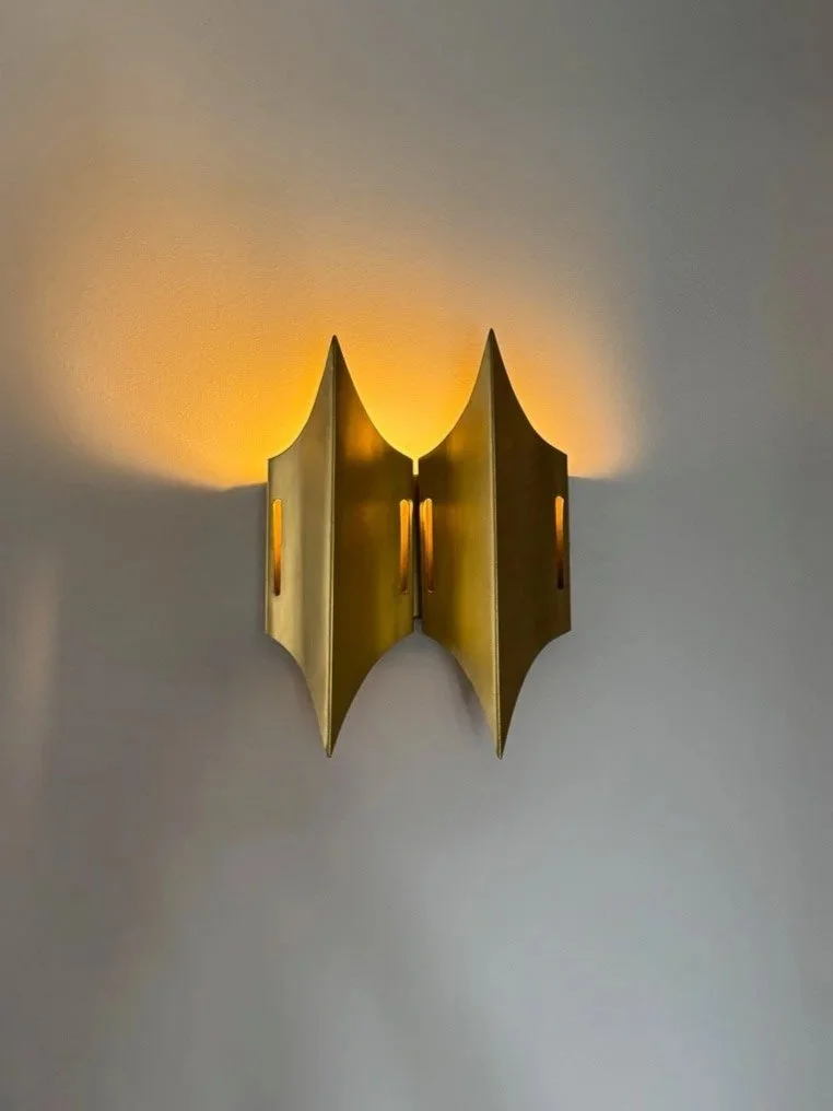 Golden wall sconce with a modern design, casting a warm glow on the wall.