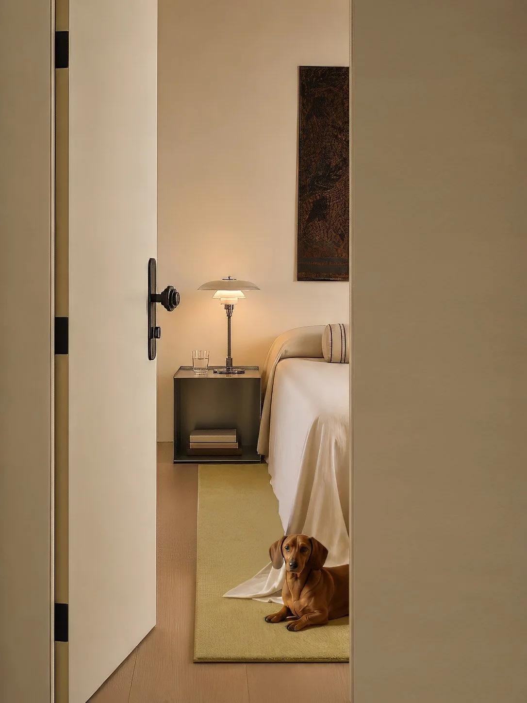 View through a doorway to the bedroom, a dachshund resting on a chartreuse rug beside the bed