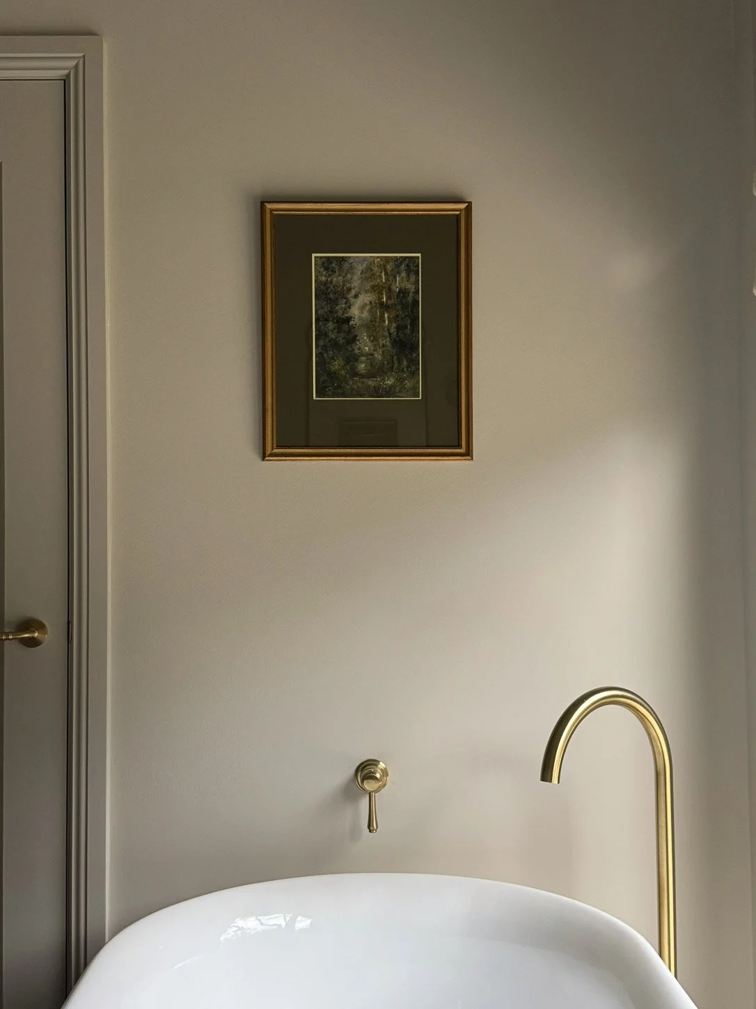 Freestanding bath with brass floor-mounted tap below a gold-framed landscape painting